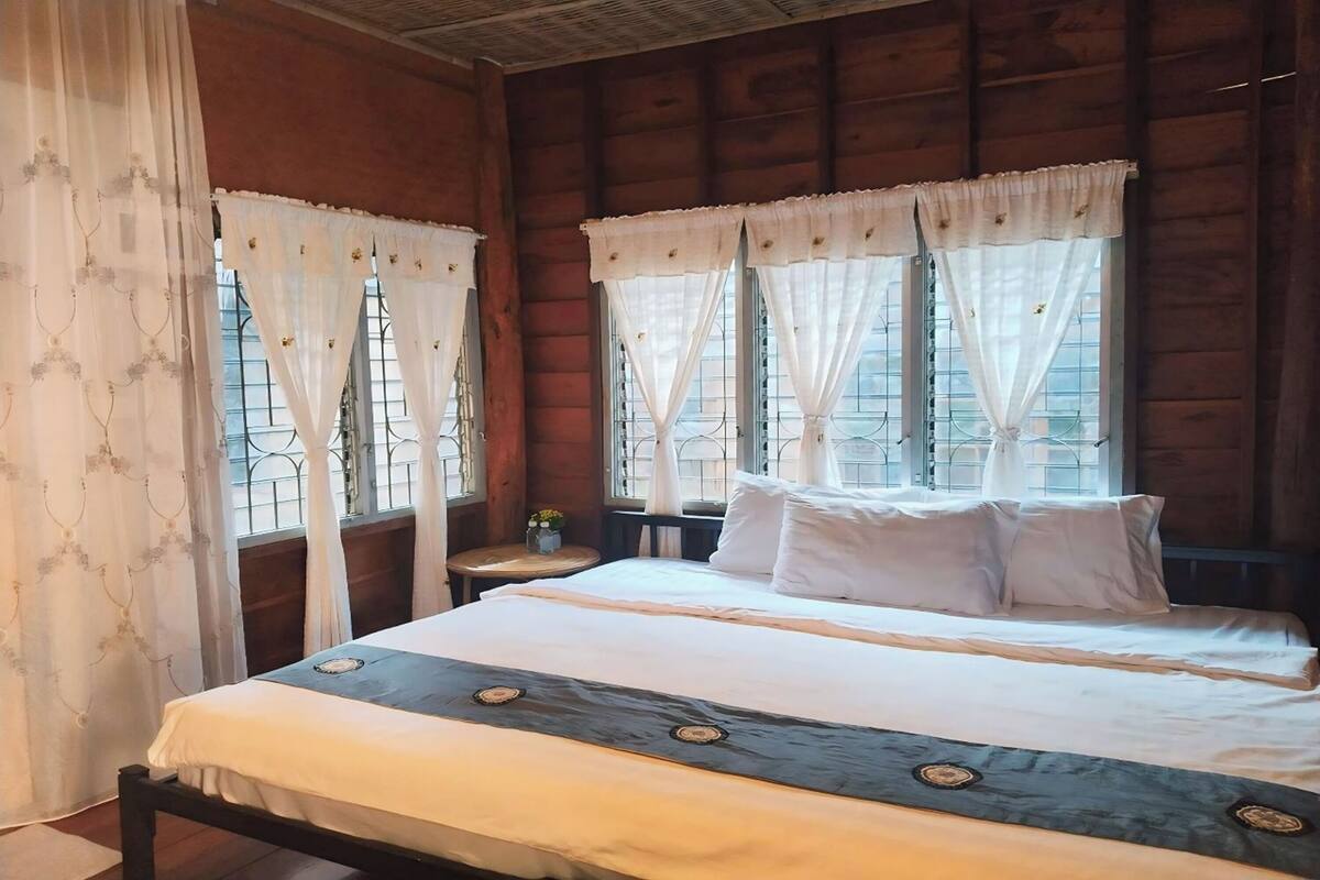 Habitación de cabaña de madera con dos camas, ropa de cama blanca y cortinas con estampado floral.