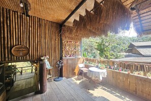 Une terrasse en bois avec un toit de chaume, des murs en bambou et une petite table entourée de chaises.