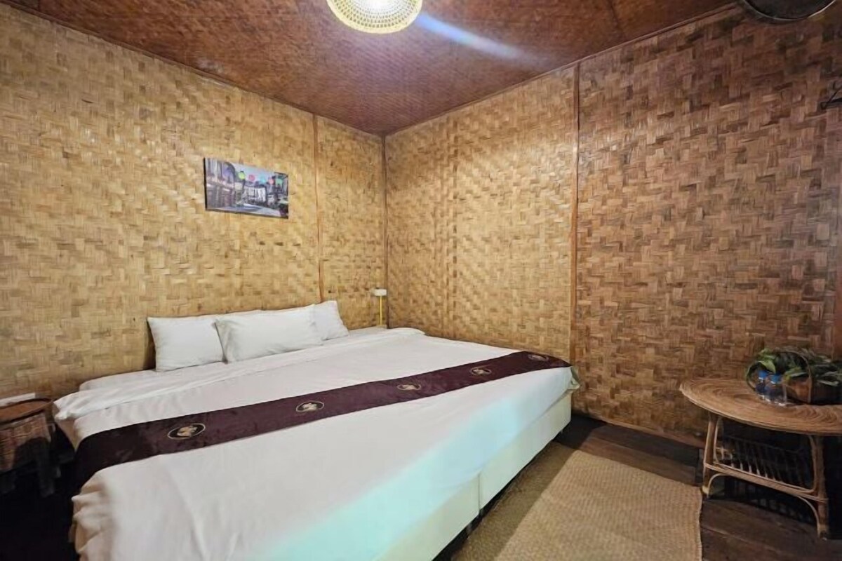 Een eenpersoonsbed met een wit en paars dekbed in een kamer met houten wanden en een geweven plafond.