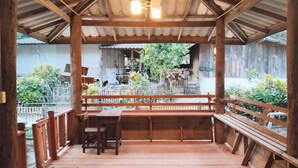 A wooden deck with benches and a table, overlooking a garden with a fence and various plants. - Mae Mae Home (Chiang Dao)