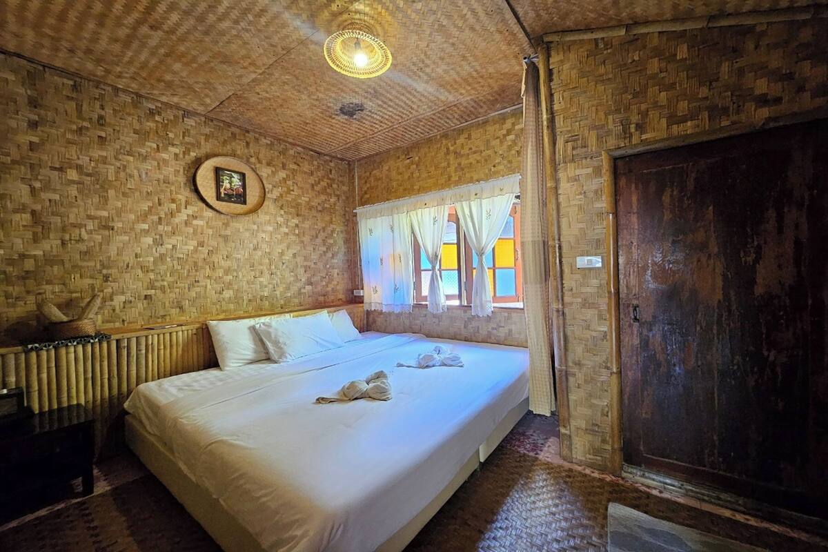 Una habitación con una cama, una puerta de madera, una ventana con cortinas y un techo tejido.