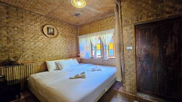 Una habitación con una cama, una puerta de madera, una ventana con cortinas y un techo tejido.