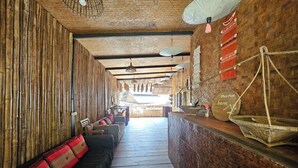 A long corridor with a wooden floor, bamboo walls, and a reception desk with a sign reading "Mccartney home". - Mae Mae Home (Chiang Dao)