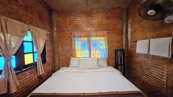 A room with a bed, curtains, a fan, and a window with patterned curtains.