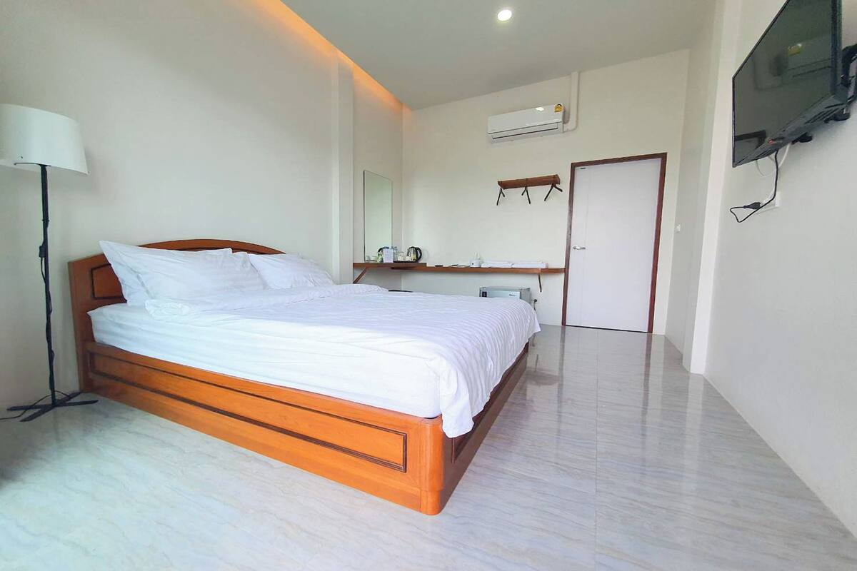 A bedroom with a wooden bed, a bedside table, a lamp, a TV mounted on the wall, and an air conditioning unit.