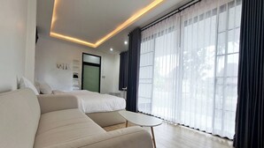 Moderni hotellihuone, jossa on sohva, pieni pöytä, sänky ja suuret ikkunat, joissa on läpikuultavat verhot.