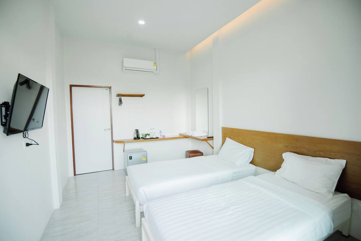 A hotel room with two beds, a TV, an air conditioner, a desk with a chair, and a mirror.