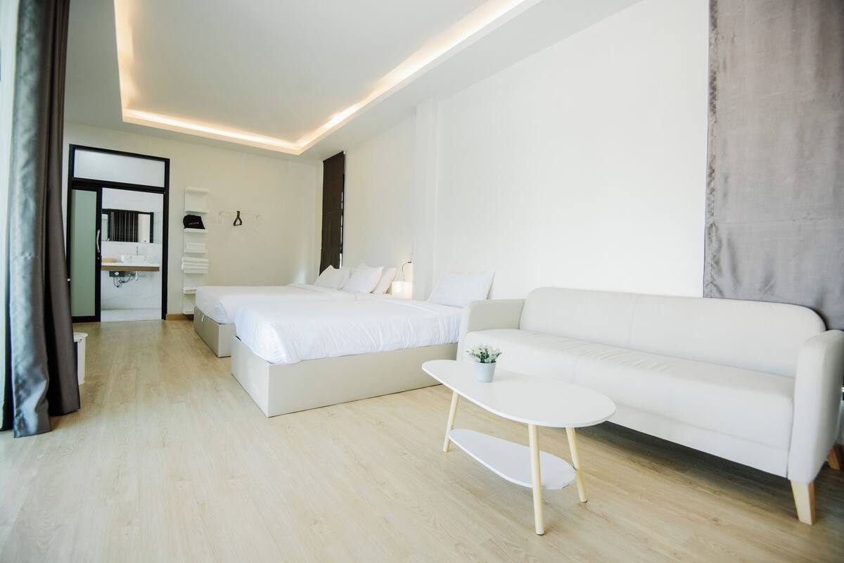 A modern hotel room with a large bed, a sofa, a small table, and a bathroom visible through an open door.