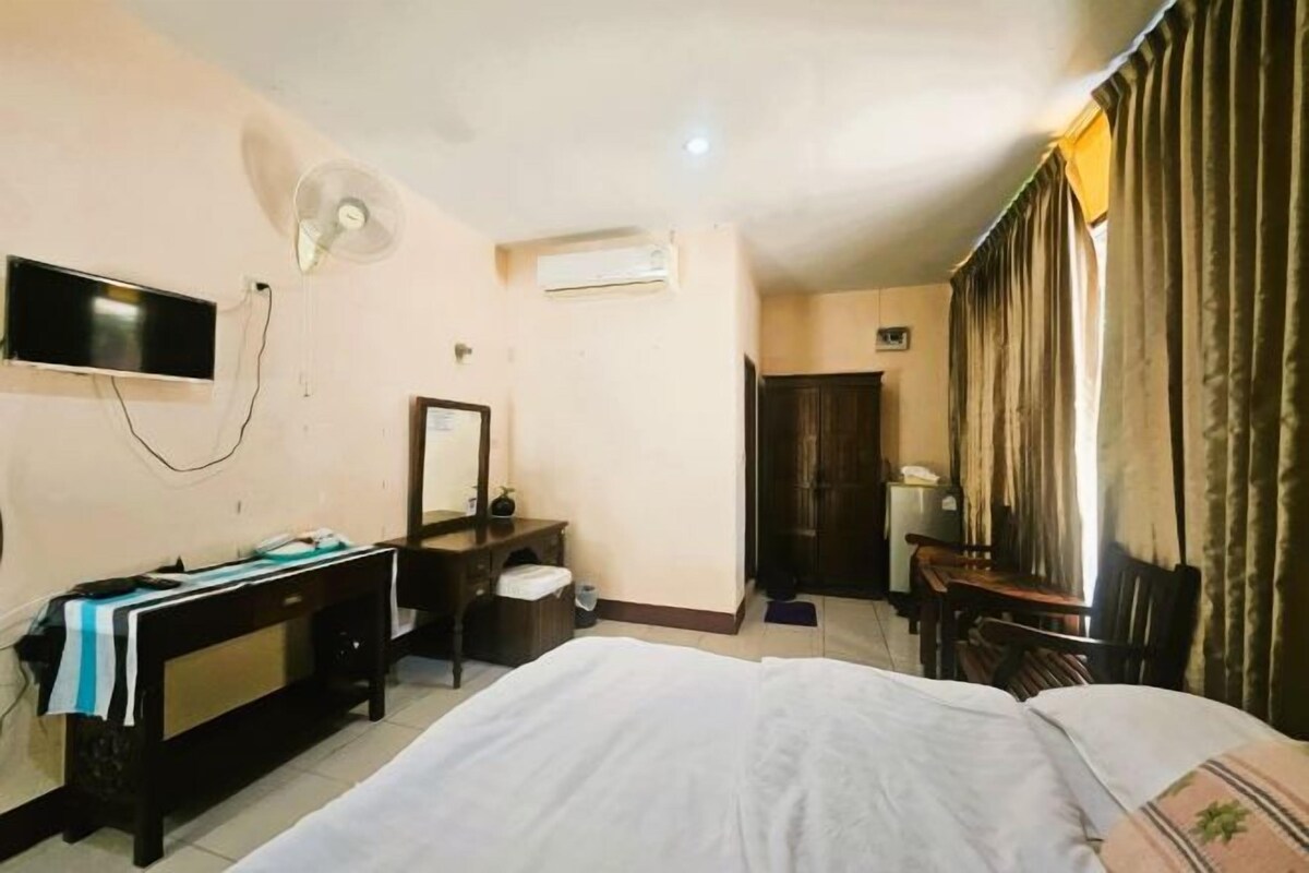 Ein Hotelzimmer mit einem Bett, einem Schreibtisch, einem Stuhl, einem Fernseher, einer Klimaanlage und einem Vorhangfenster.