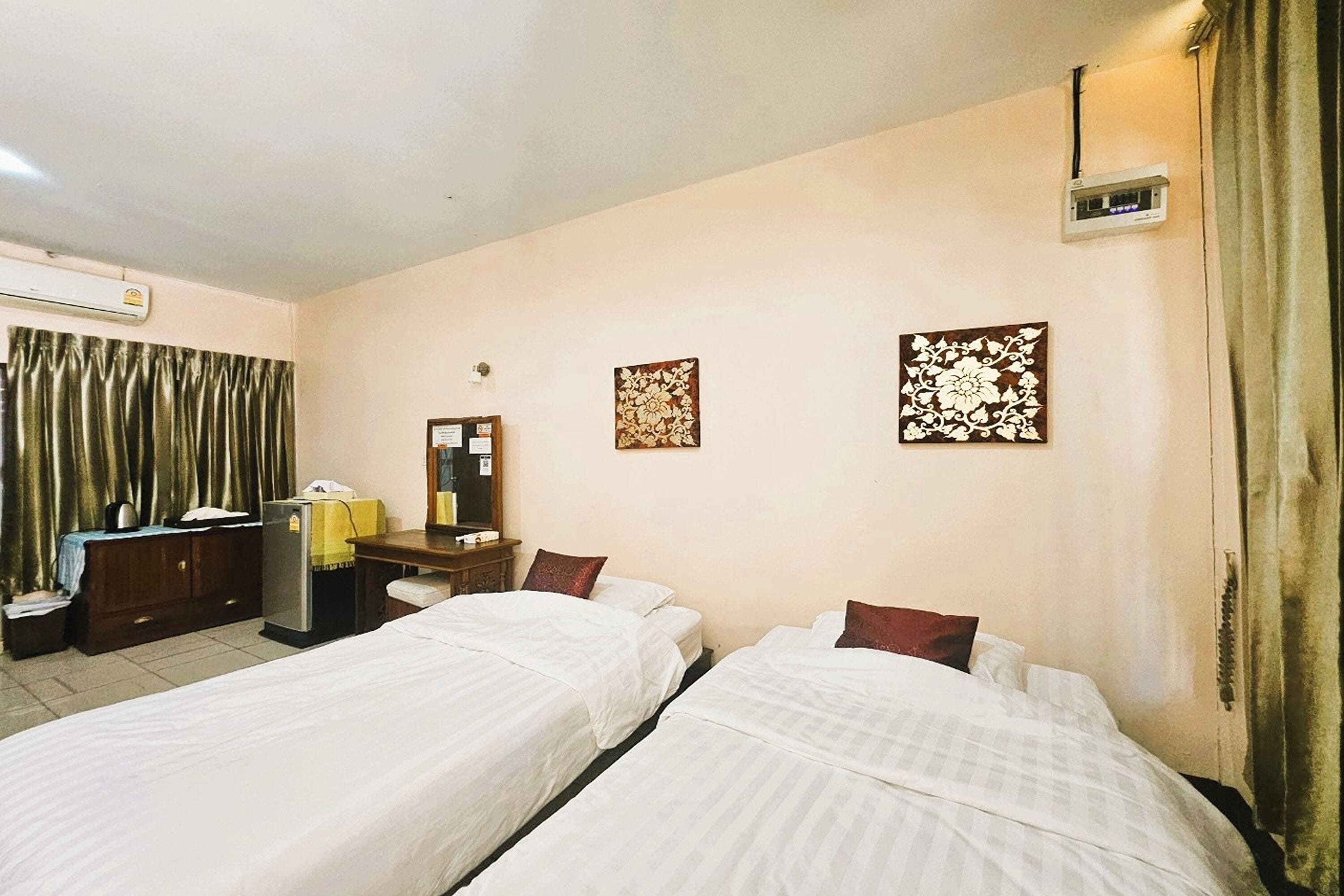 Une chambre d’hôtel avec deux lits simples, un bureau, une chaise, une armoire, un appareil de climatisation et deux éléments décoratifs muraux.