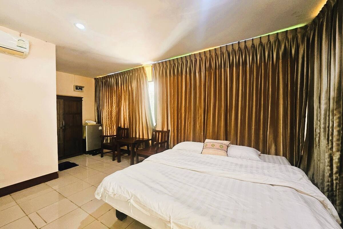 Ein Hotelzimmer mit Bett, Schreibtisch, Stuhl, Kühlschrank und Vorhängen.