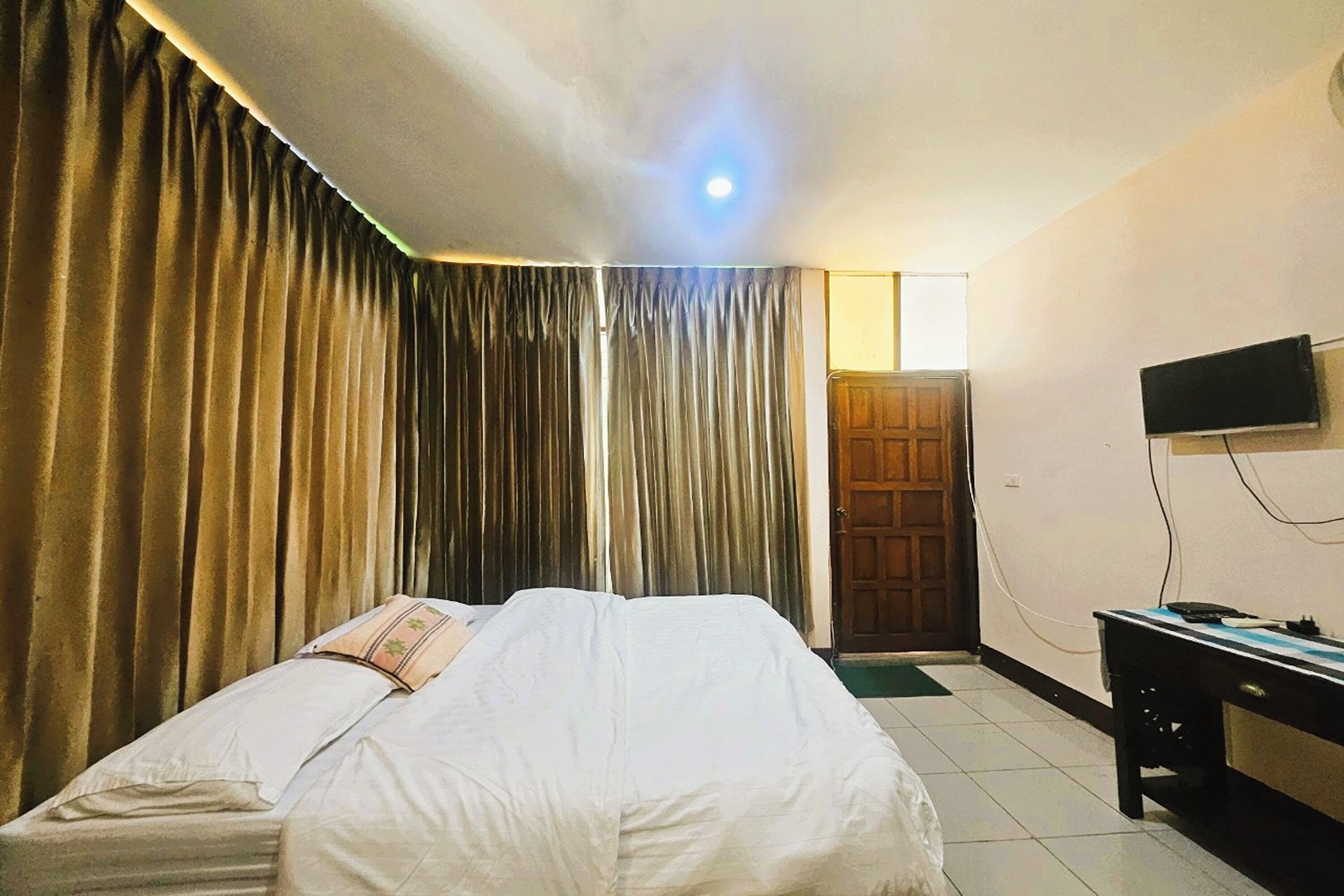 A hotel room with a bed, curtains, a television, and a desk.