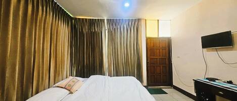 A hotel room with a bed, curtains, a television, and a desk.