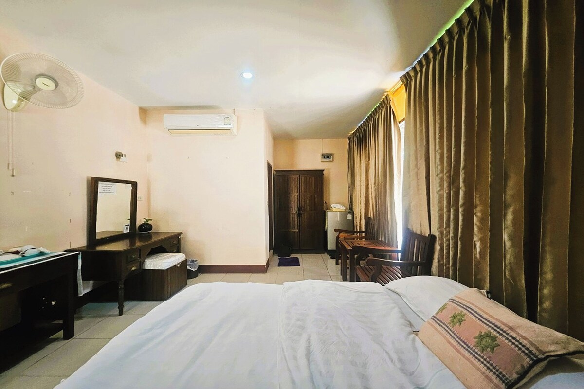 Une chambre d’hôtel équipée d’un lit, d’un bureau, d’une chaise, d’un miroir, d’un ventilateur et de rideaux.