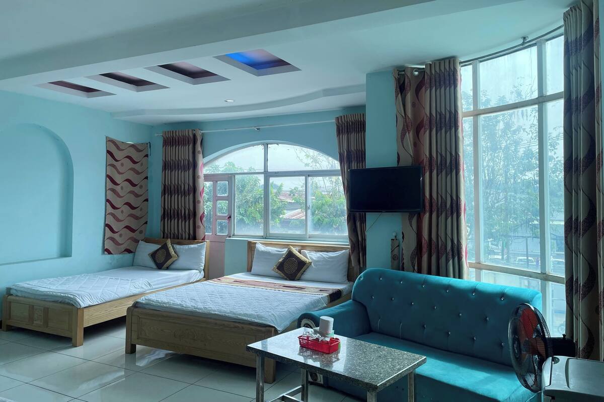 A room with two beds, a sofa, a TV, and a window with curtains.