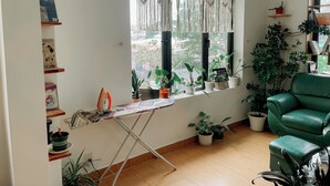 Une pièce dotée d’une grande fenêtre, d’un fauteuil vert et de plusieurs plantes en pot.