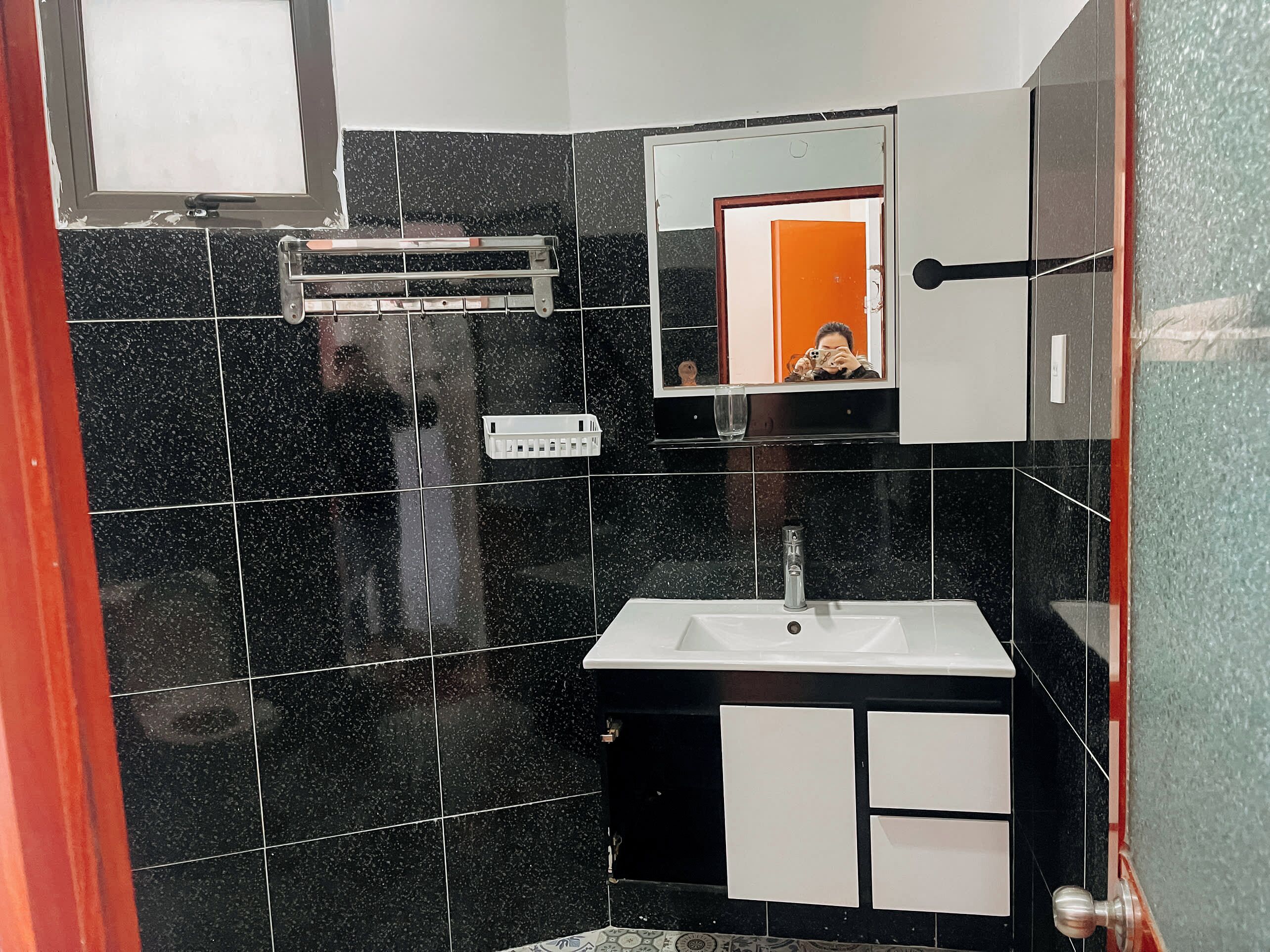 A bathroom with black speckled tiles, a white sink, a mirror, and a towel rack.