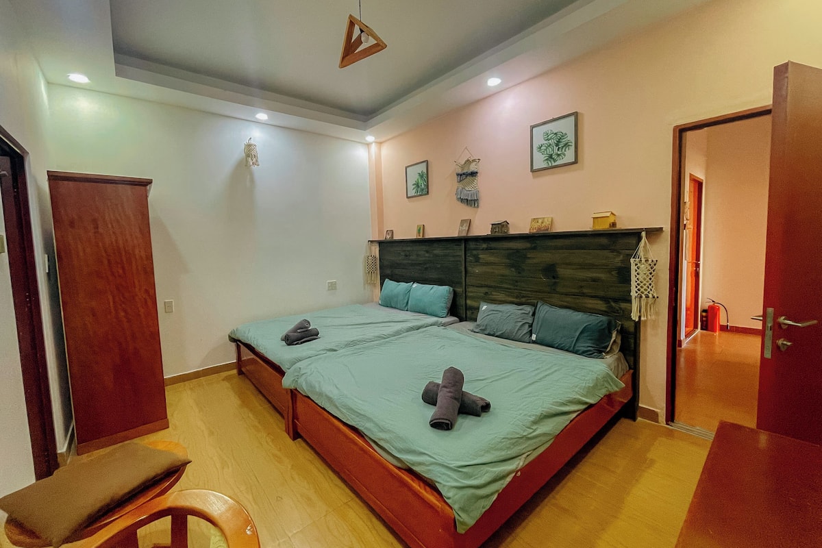 A bedroom with two beds, a wooden bench, and a door.