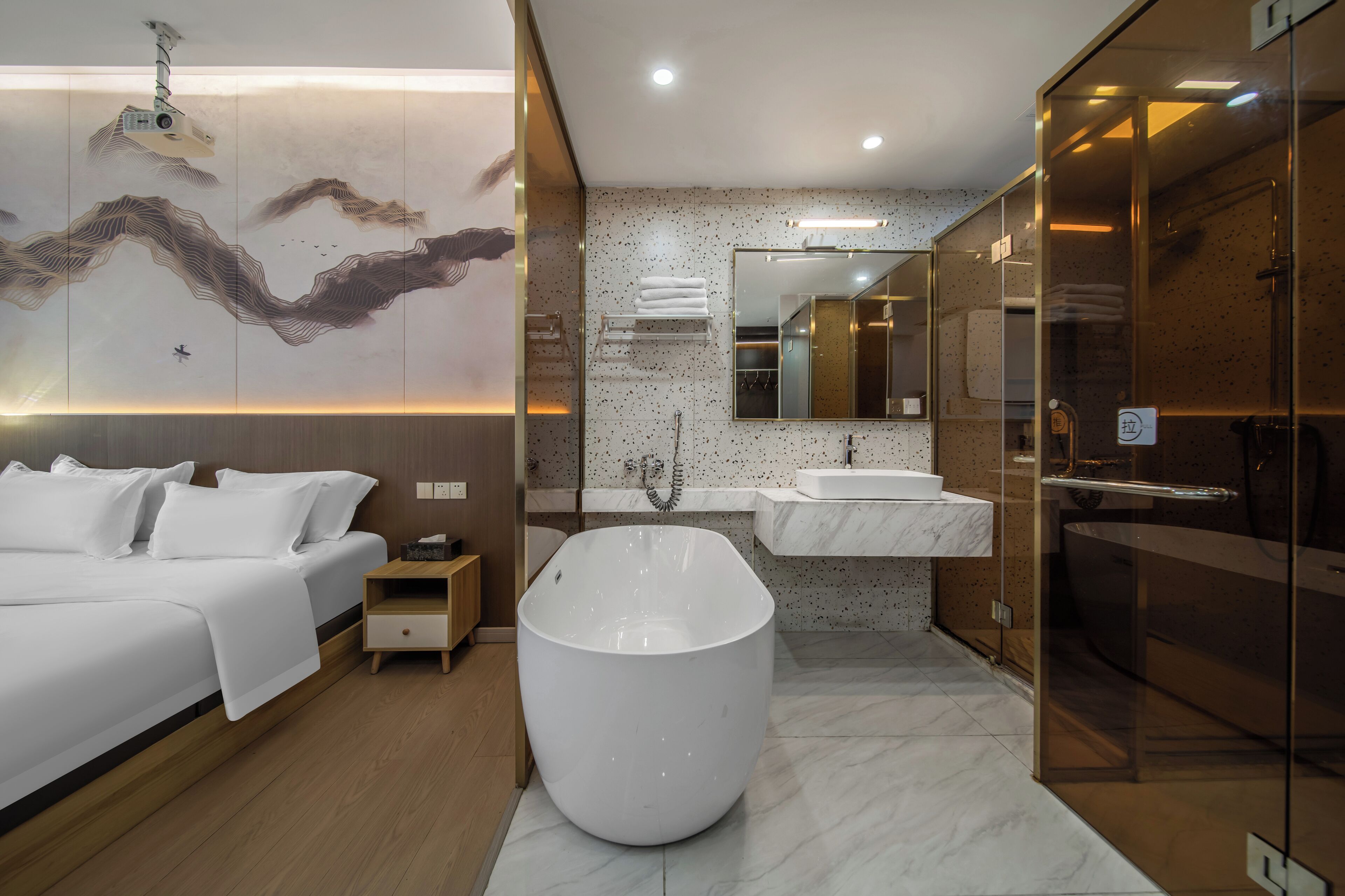 Una habitación de hotel moderna con una cama grande, una bañera independiente, una ducha con cerramiento de vidrio y un lavamanos montado en la pared.