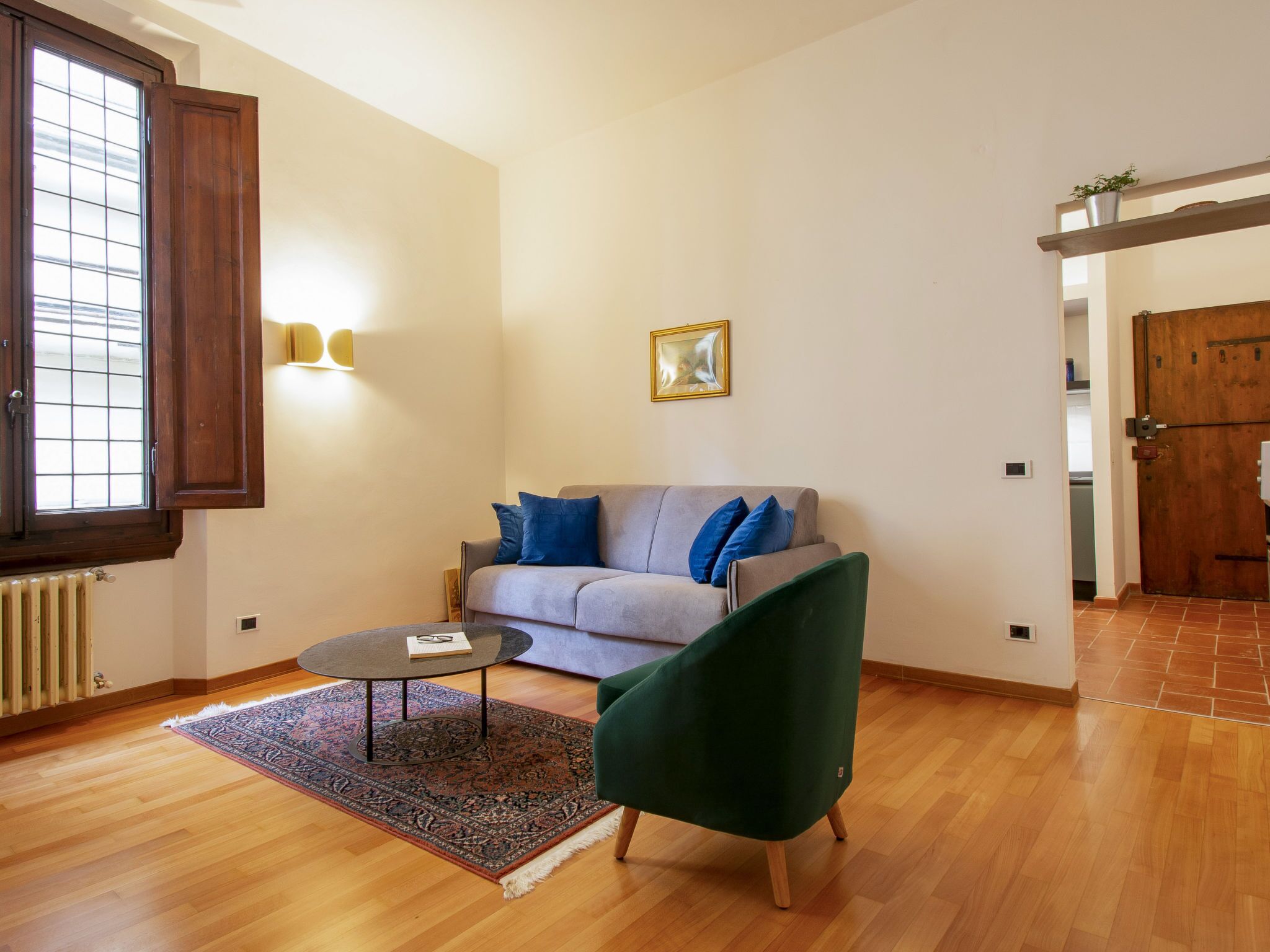 Ein Wohnzimmer mit grauem Sofa, einem grünen Sessel, einem runden Couchtisch und einem Teppich mit Muster.