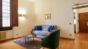 Uma sala de estar com um sofá cinza, uma poltrona verde, uma mesa de centro redonda e um tapete estampado.