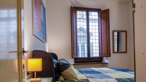 Quarto com cama, mesa de cabeceira, luminária, janela com cortinas e espelho.