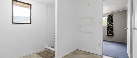 A room with white walls, a tiled floor, a window with a view, and a door leading to another room.