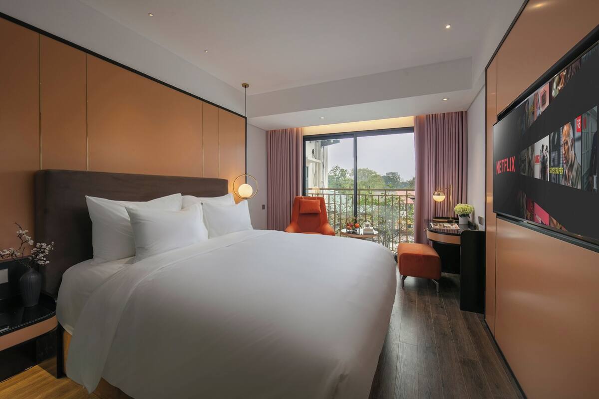 A modern hotel room with a large bed, a desk, a chair, and a TV displaying Netflix content.