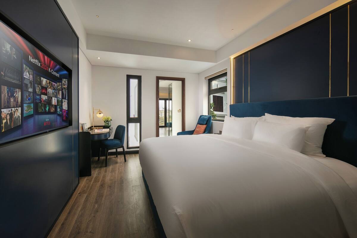A modern hotel room with a large bed, a desk, and a wall-mounted TV displaying Netflix content.