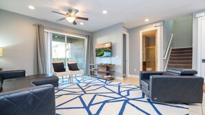A modern living room with a large sectional sofa, a flat-screen TV, a ceiling fan, and a staircase leading to an upper level. - Classic 8-bedroom house with AC, WiFi in Kissimmee - Encore Reunion (Kissimmee)
