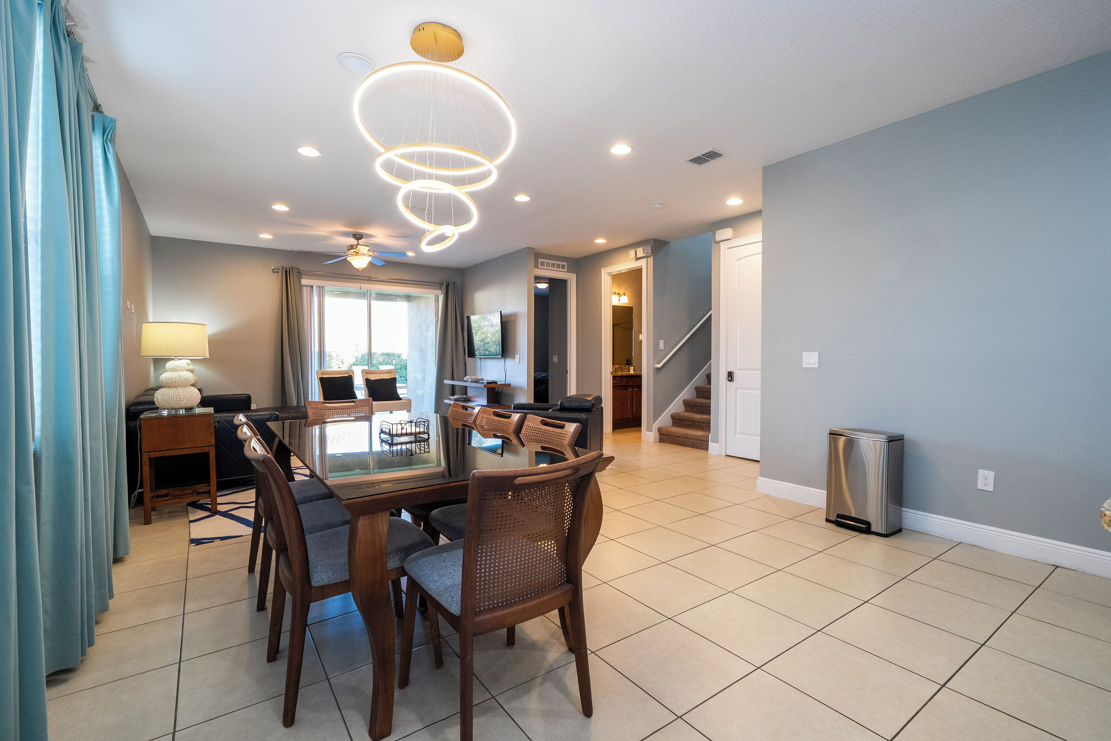 A spacious dining area with a modern chandelier, wooden chairs, and a large table.