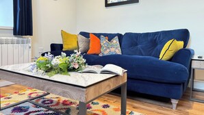 Un salon avec un canapé bleu, des coussins colorés, une horloge et un tableau accroché au mur.