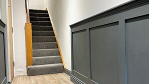 Un escalier dont les marches sont recouvertes de moquette et qui possède des rampes en bois, menant à un palier avec un mur foncé et un plancher de couleur claire.
