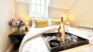 Une chambre d’hôtel avec un lit, une table de chevet ornée d’un vase de fleurs, une bouteille de vin et des verres disposés sur un plateau.