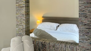 A hotel room with a bed, a wall-mounted mirror, and a stack of books on the wall. - Warehouse Apartments (Ulverston)
