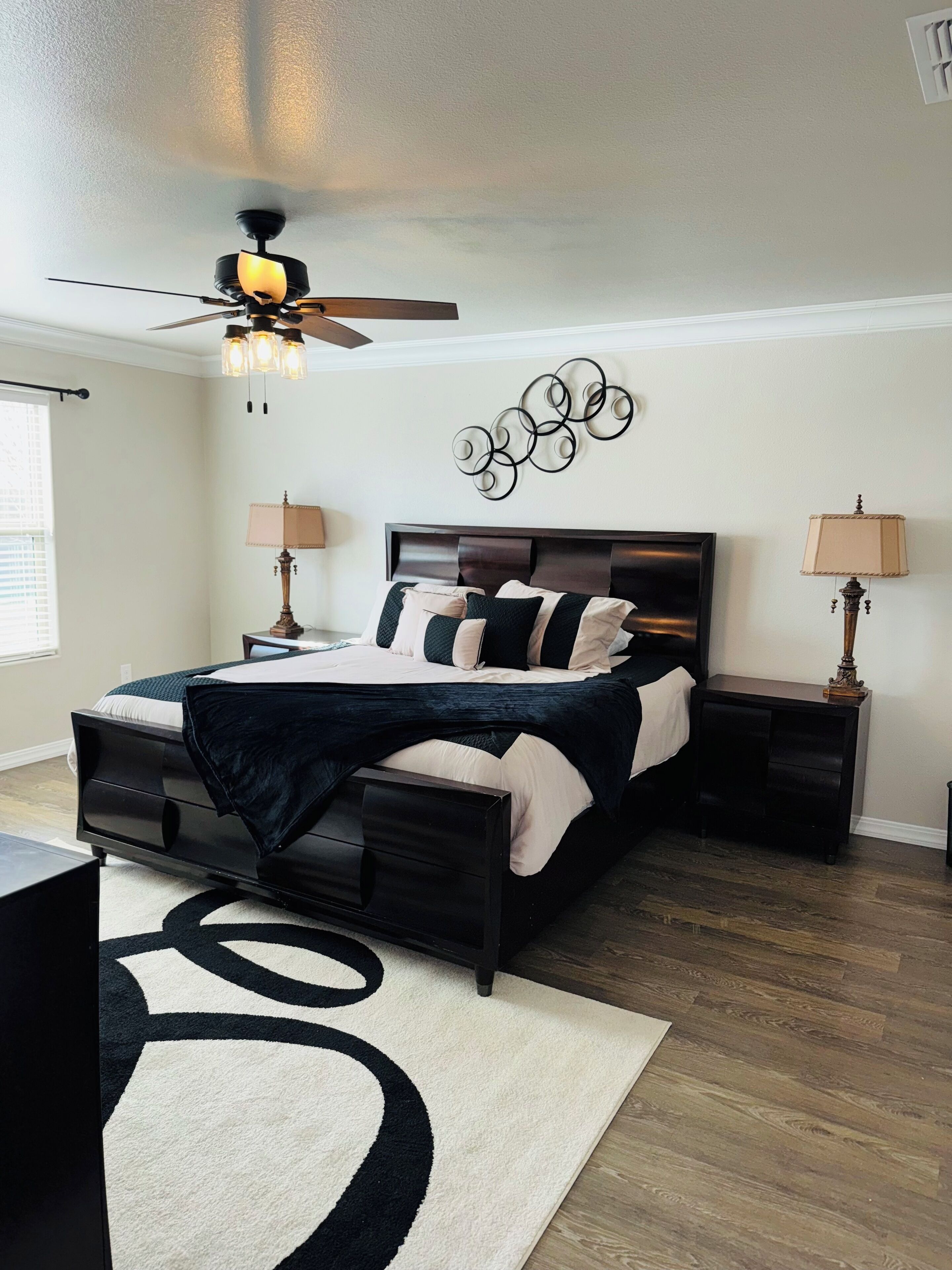 A bedroom with a bed, nightstands, a ceiling fan, a wall art piece, and a rug.