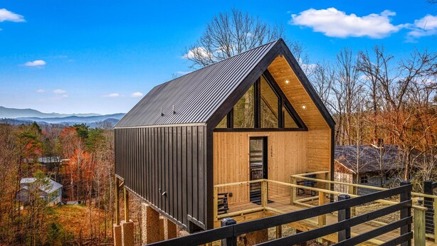Una moderna baita con facciata in legno e tetto in metallo, con un balcone e vista panoramica sulle montagne.