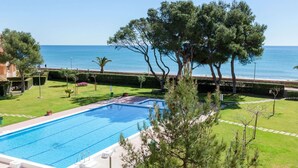 A swimming pool with a view of the sea, surrounded by well-maintained grass and trees.