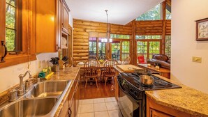 Cocina de cabaña de madera con armarios de madera, encimera de granito, un lavabo, estufa y comedor con sillas y una mesa.