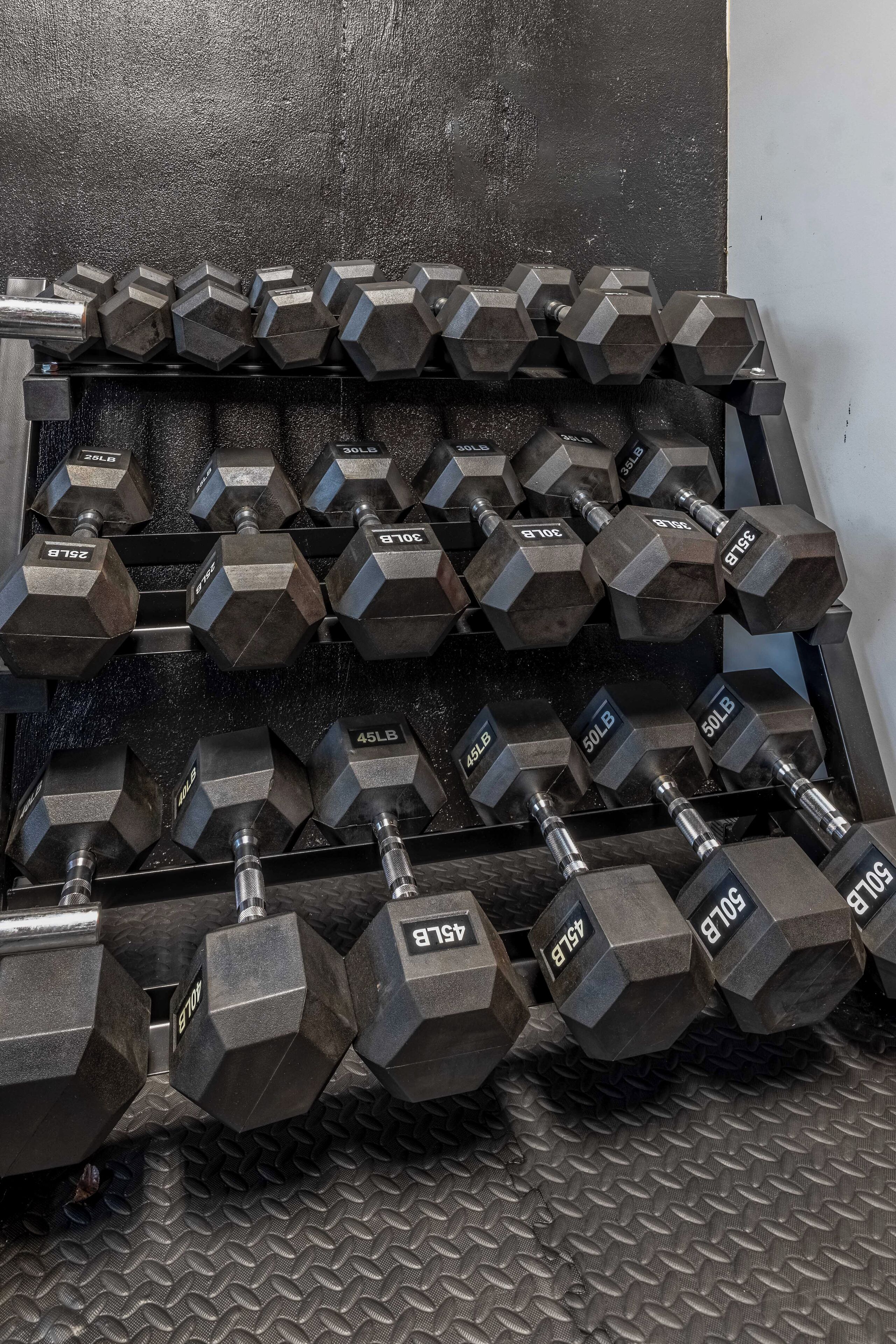 A rack of hexagonal dumbbells with weight markings, arranged on a textured floor.