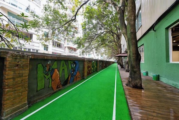 A narrow pathway with green artificial turf, a brick wall with colorful graffiti, and a tree-lined sidewalk. - Fuzhou Rongtong Meifeng Hotel (Fuzhou)