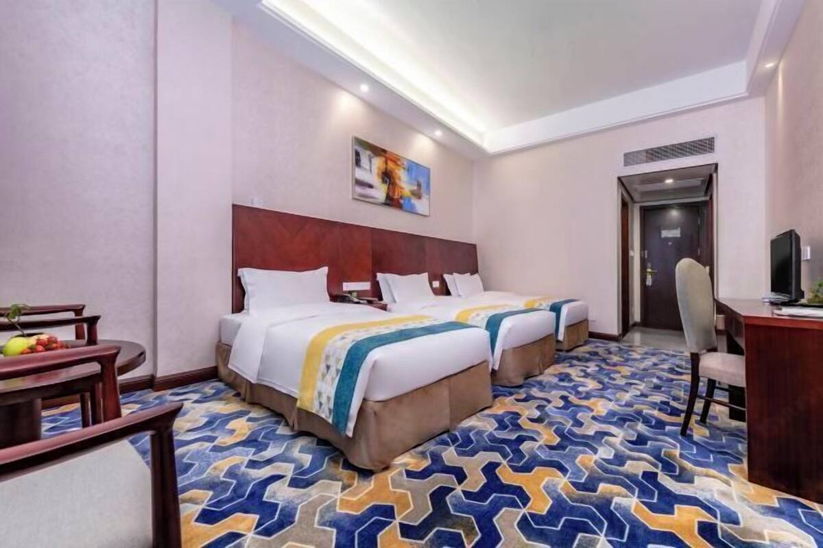 A hotel room with two beds, a desk, a chair, and a dining table.
