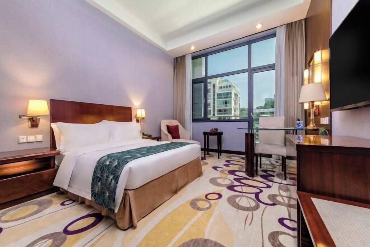 A hotel room with a large bed, a desk, a chair, and a TV.