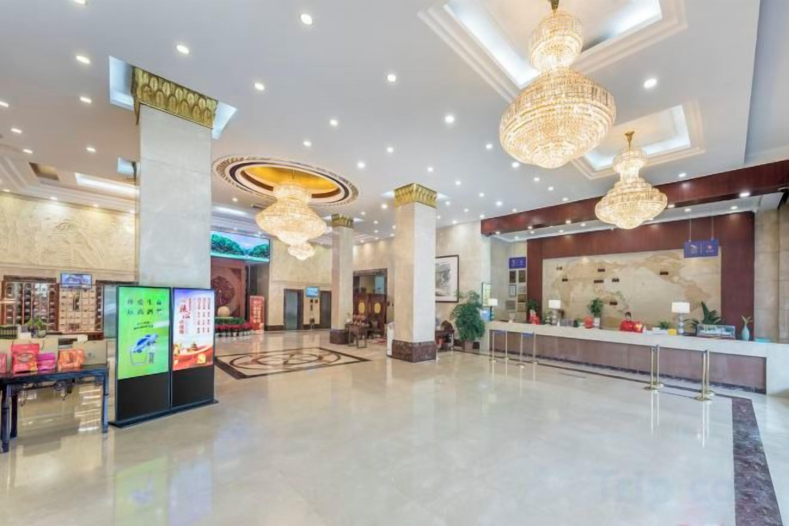 A spacious lobby with a reception desk, digital information kiosks, and decorative chandeliers.