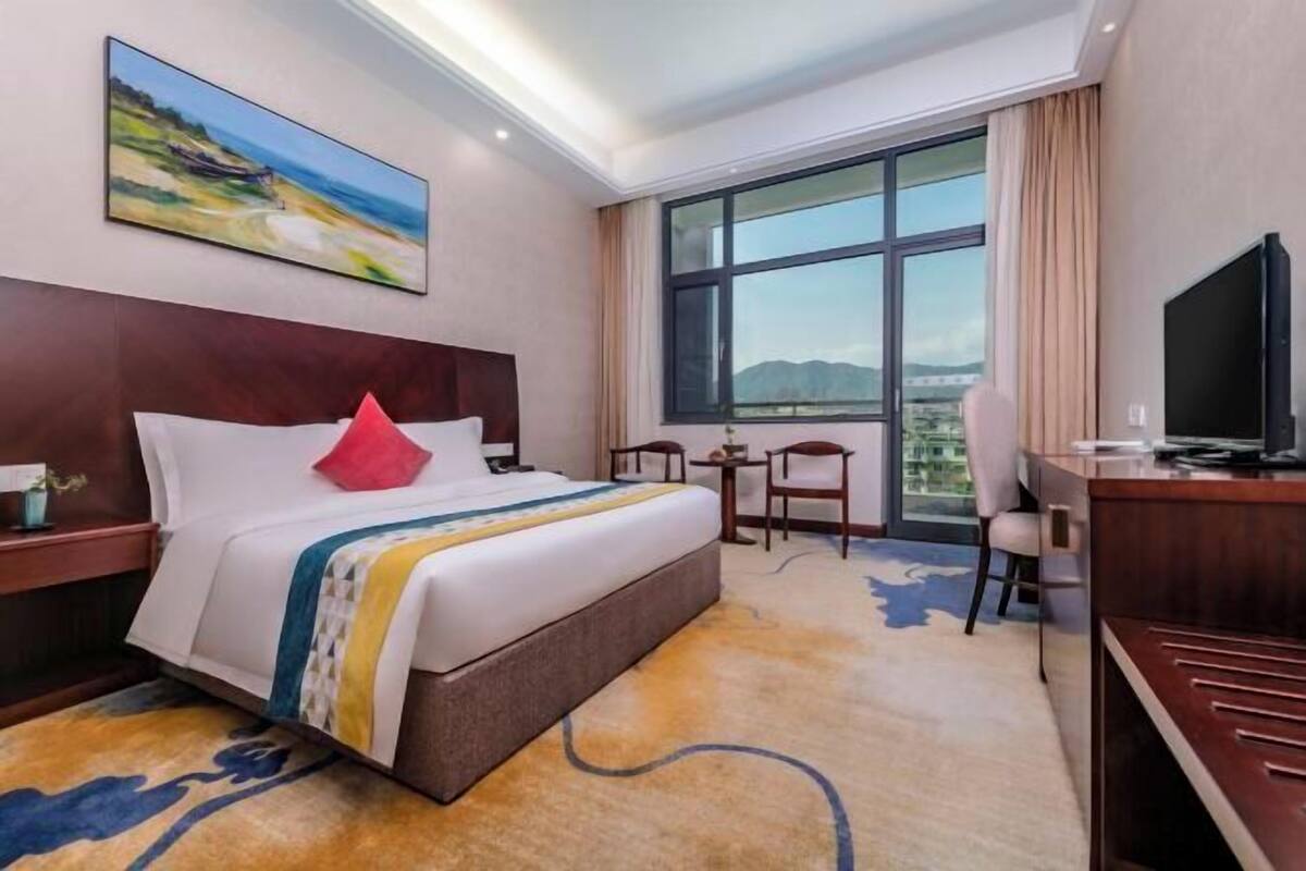A hotel room with a large bed, a desk, a chair, a TV, and a window with a view of the mountains.