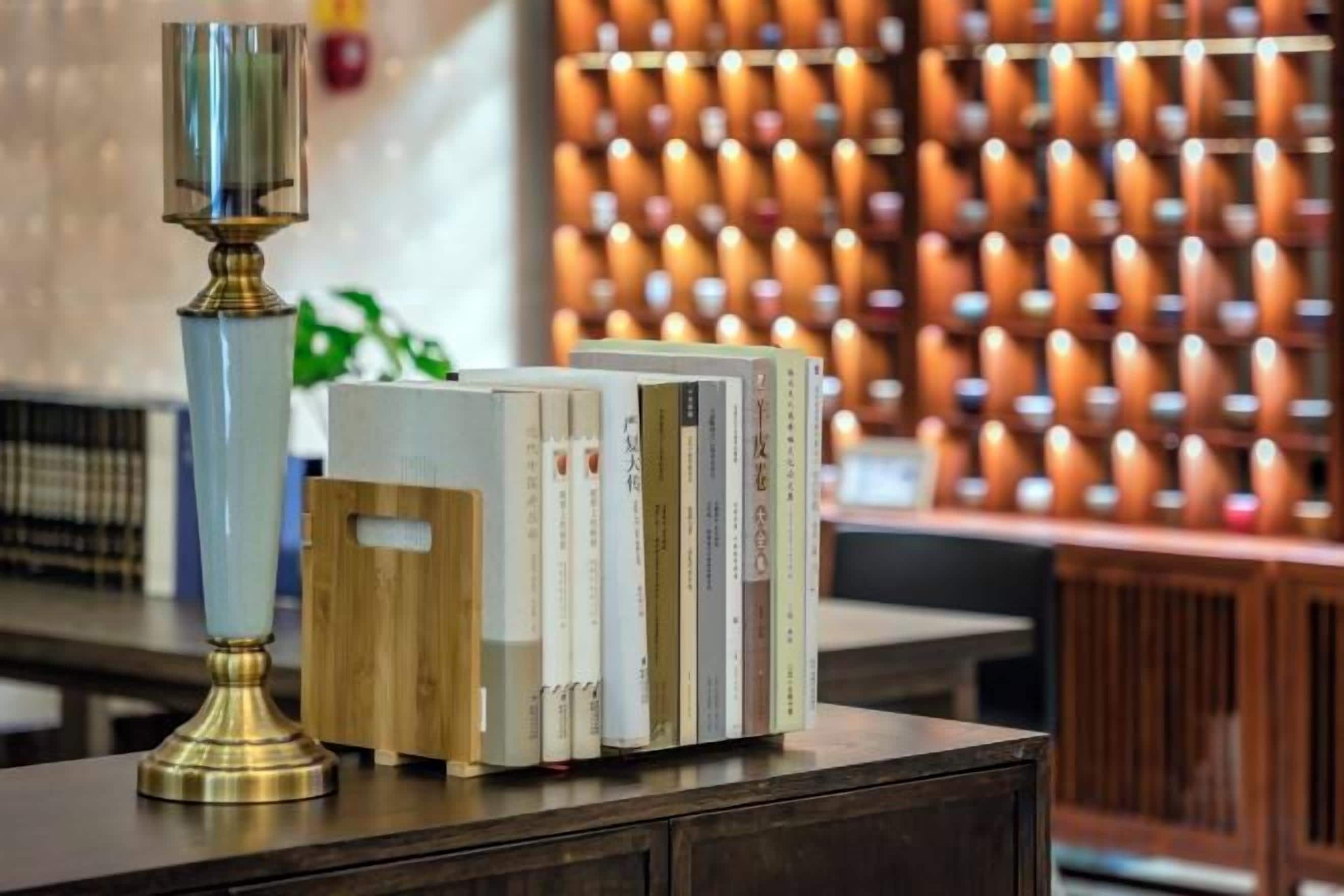 A stack of books on a wooden surface with a tall, slender lamp beside them.