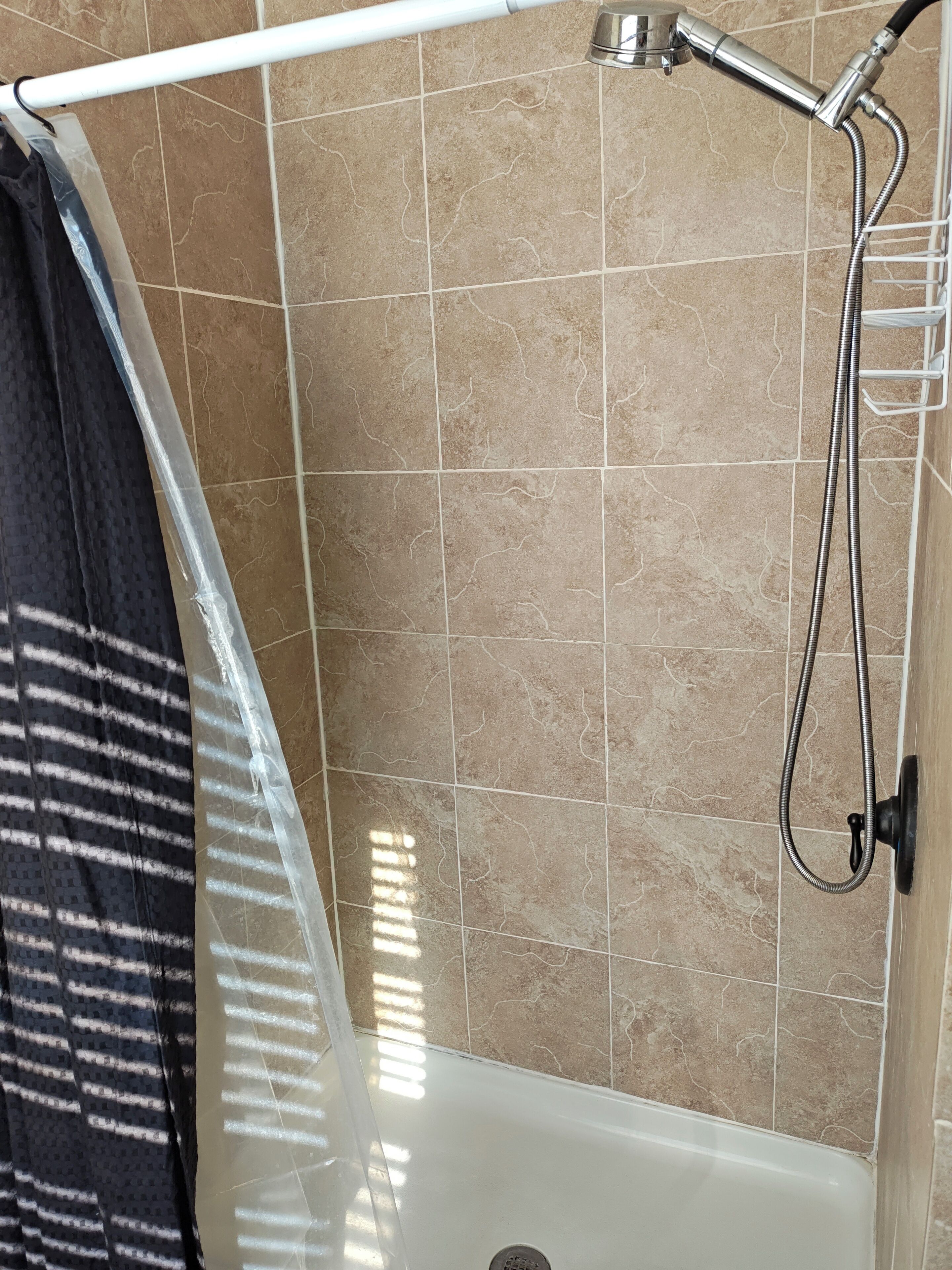Ein Duschbereich mit einer weißen Badewanne, einer Duschbrause und einem Handtuchhalter.