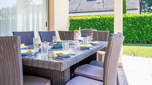 Un espace de restauration en plein air avec une table à plateau de verre, des chaises en osier et une table soigneusement dressée avec des assiettes, des verres et des couverts.