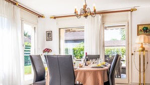 Un coin repas avec une table dressée pour quatre personnes, des chaises, un lustre et une vue sur l’extérieur.