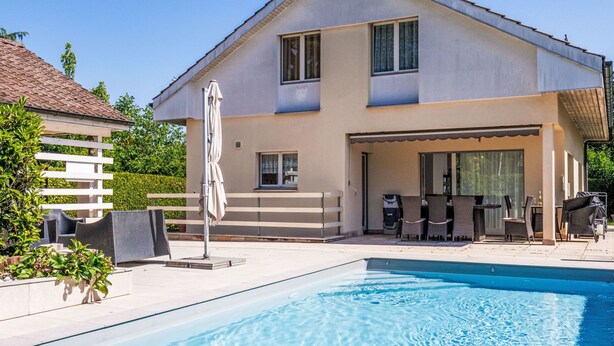 Une maison à deux étages dotée d’une piscine, de mobilier d’extérieur et d’un patio couvert.
